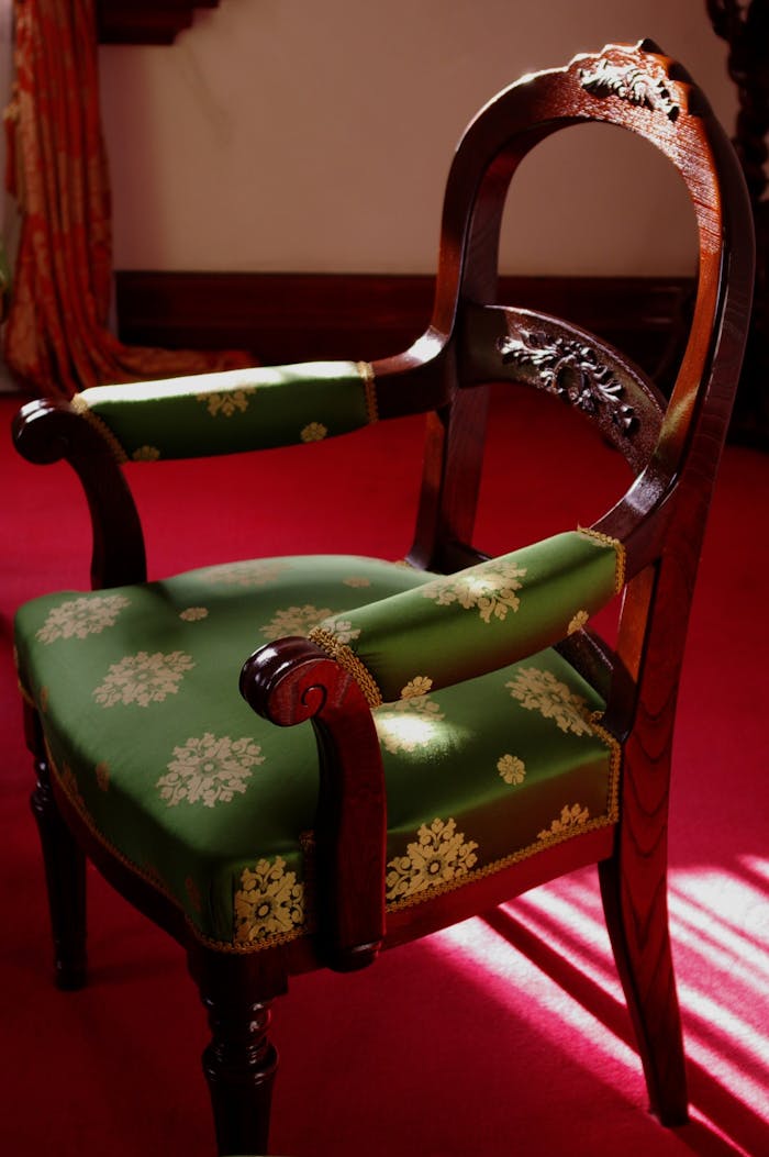 Elegant antique armchair with ornate wooden design and green floral upholstery in warm lighting.